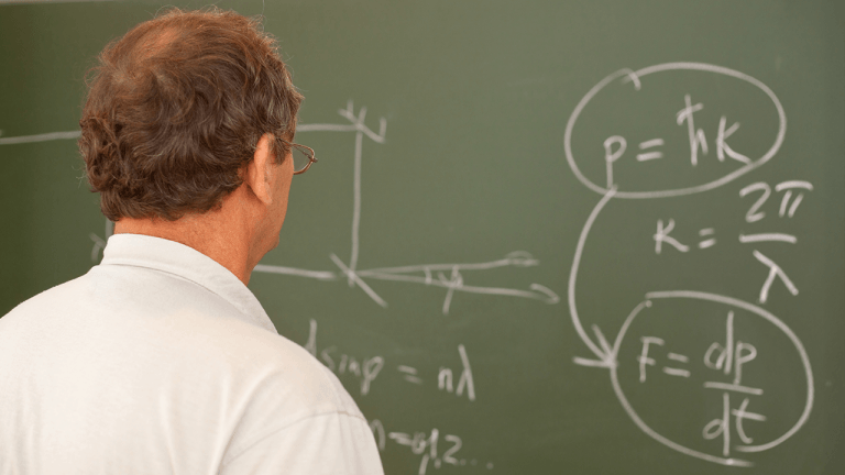 A professor studies equations on a chalkboard covered with mathematical formulas.